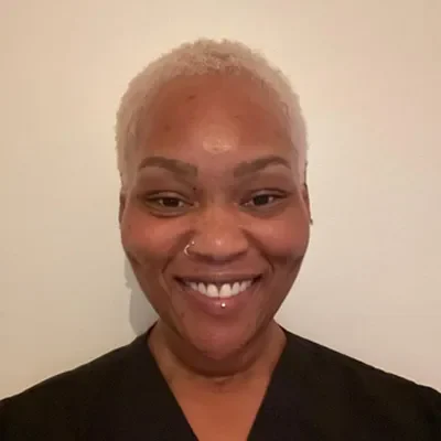 Massage Therapist Alpharetta GA Taylor Patrick Meet The Team Massage Therapist, Taylor standing against a beige wall. She is smiling